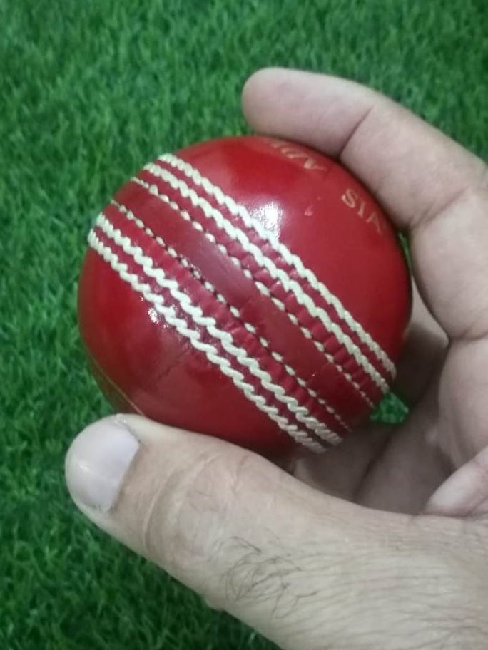A red leather cricket ball from the "Advance Target 300 - 156g Red - Pack of 6 Balls" collection is featured against a plain white background, showcasing its prominent white hand-stitching. The ball boasts the brand name "ADVANCE" engraved in gold letters on one side, emphasizing its premium quality.