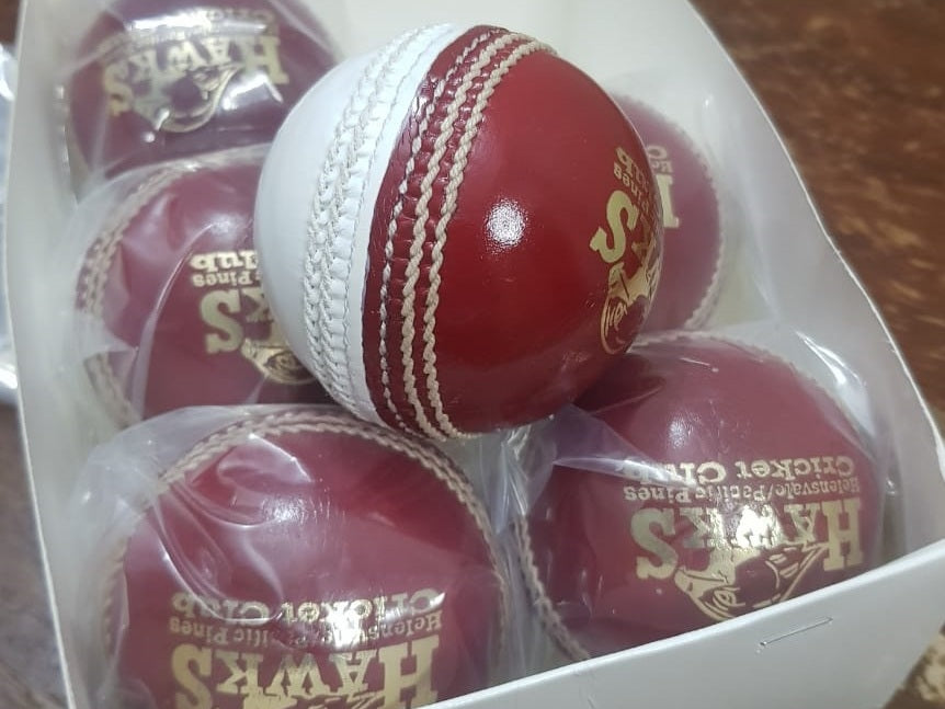 A close-up image of a Super Match 156g Dual Color cricket ball by Advance, featuring red leather with white stitching. The side of the hand-stitched ball displays a logo and text, and its full cork core and leather coating give it a new, shiny appearance against the white background.