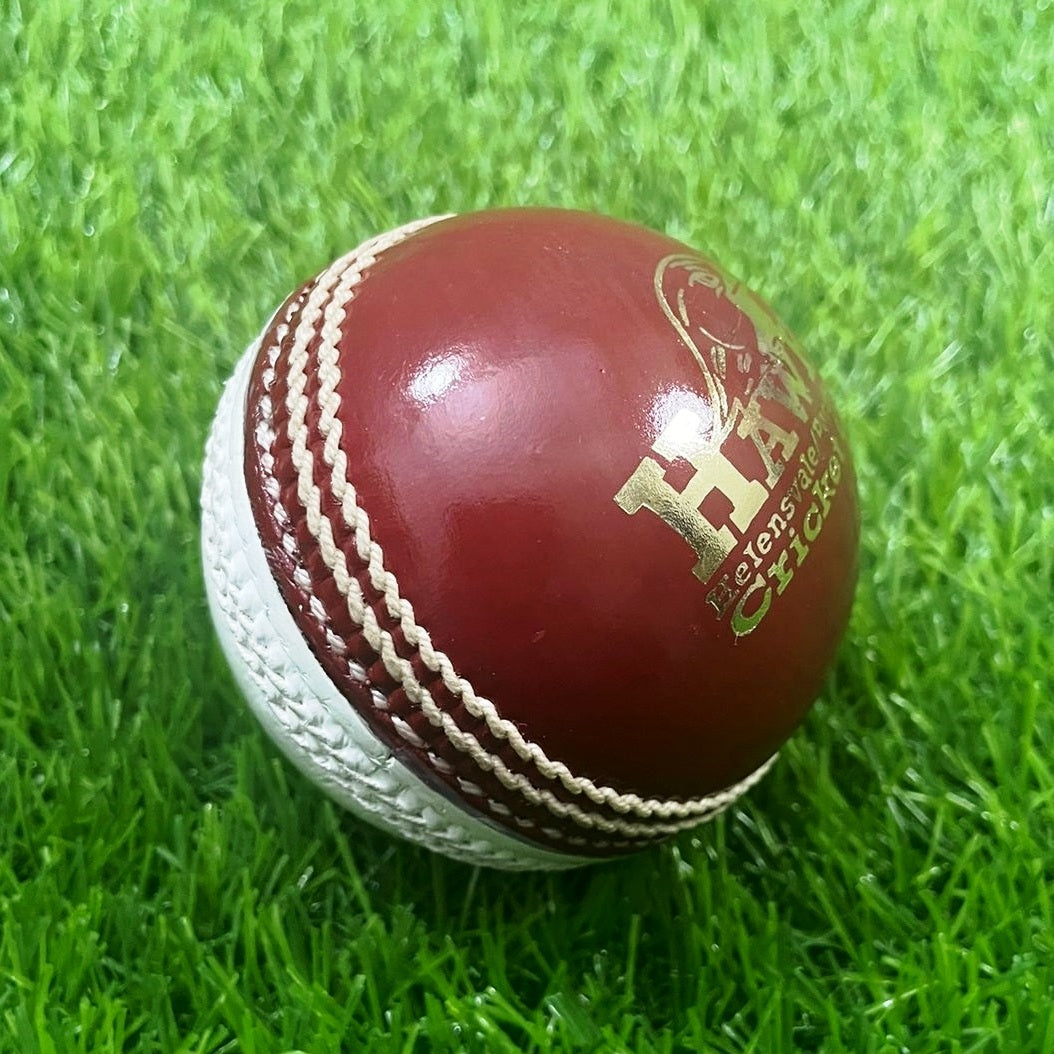 A close-up image of a Super Match 156g Dual Color cricket ball by Advance, featuring red leather with white stitching. The side of the hand-stitched ball displays a logo and text, and its full cork core and leather coating give it a new, shiny appearance against the white background.