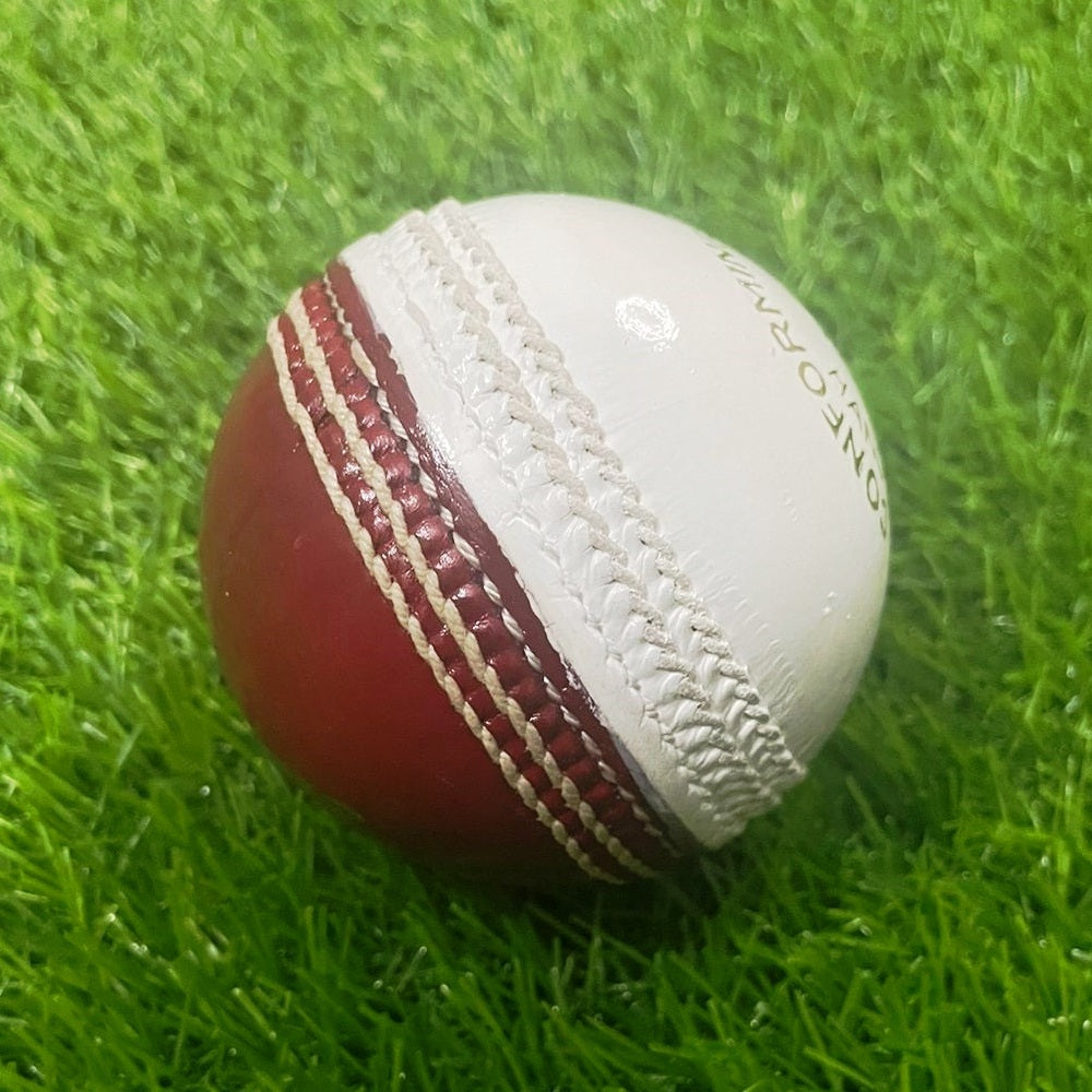 A close-up image of a Super Match 156g Dual Color cricket ball by Advance, featuring red leather with white stitching. The side of the hand-stitched ball displays a logo and text, and its full cork core and leather coating give it a new, shiny appearance against the white background.