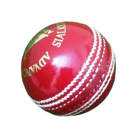 A close-up of a red leather cricket ball from the Target 1000 Super Test pack by Advance, featuring prominent white hand-stitched seams. The ball appears new and shiny with gold lettering partially visible around its circumference, displaying "STA" and "ADVAN.