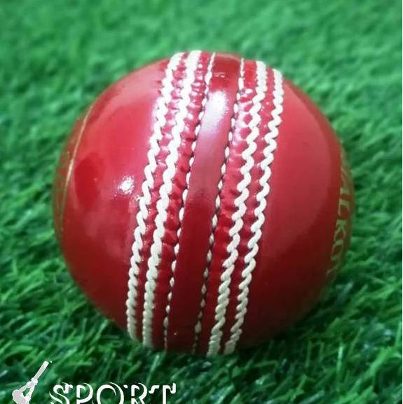 A close-up of a red leather cricket ball from the Target 1000 Super Test pack by Advance, featuring prominent white hand-stitched seams. The ball appears new and shiny with gold lettering partially visible around its circumference, displaying "STA" and "ADVAN.