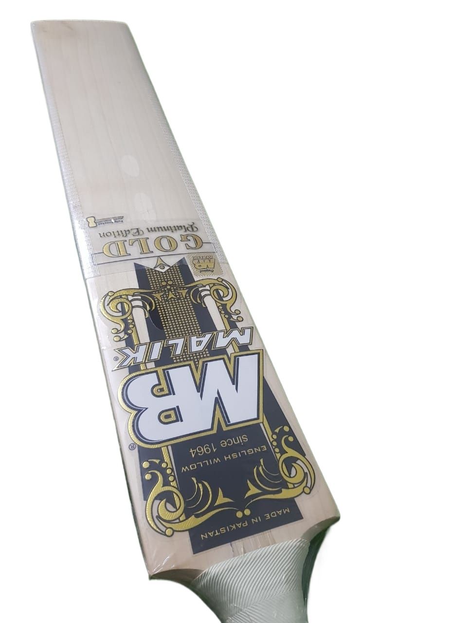 Two MB Malik Gold cricket bats, expertly crafted from professional standard pro grade English Willow, are standing side by side. The left bat displays the front featuring the "MB Malik Gold" name and decorative designs. The right bat reveals the back with "MALIK" written vertically in bold letters. Both bats are equipped with black handles.