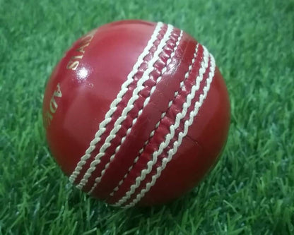 a close view of a red hand-stitched cricket ball "Advance - Target 300" on the ground.